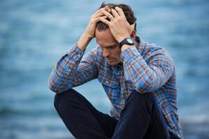 Microdiscectomy Journey A man in a plaid shirt sits by the water looking distressed, symbolizing stress.